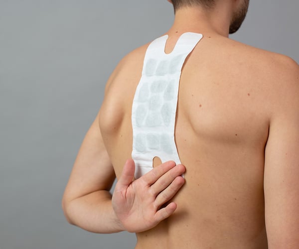 Mann mit freien Oberkörper fixiert ThermaCare® Wärmeauflage für größere Schmerzflächen mit dem Handrücken von unten auf der Haut