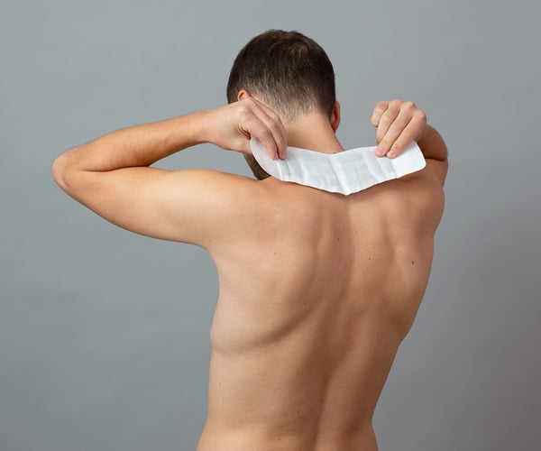 Mann mit freiem Oberkörper klebt sich ThermaCare® Wärmeauflage auf den Nacken
