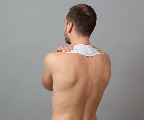 Mann mit freiem Oberkörper fixiert ThermaCare® Wärmepflaster am Nacken 