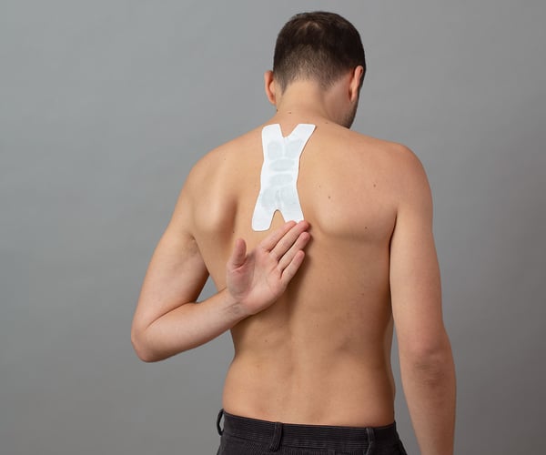 Mann mit freien Oberkörper fixiert ThermaCare® Wärmeauflage für flexible Anwendung mit dem Handrücken