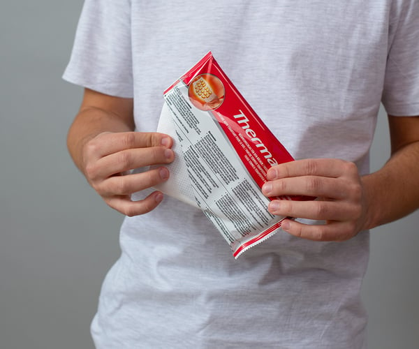 Person in weißem T-Shirt öffnet Verpackung der ThermaCare® Wärmeumschläge für den Rücken