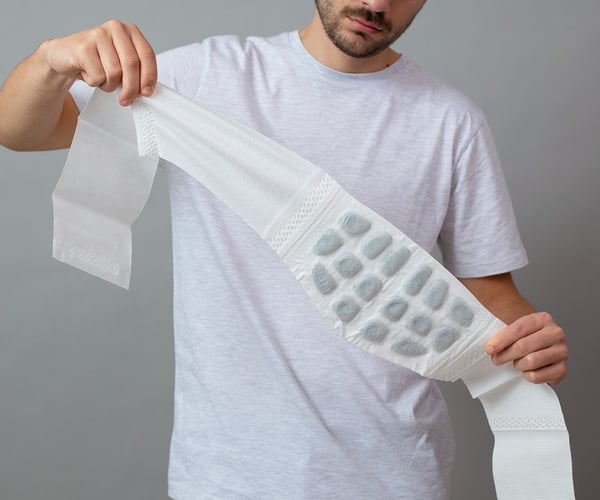Mann in weißem T-Shirt klappt ThermaCare® Wärmeumschlag bei Rückenschmerzen komplett aus