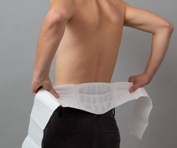 Mann mit freiem Oberkörper legt ThermaCare® Wärmeumschlag gegen Rückenschmerzen von hinten um