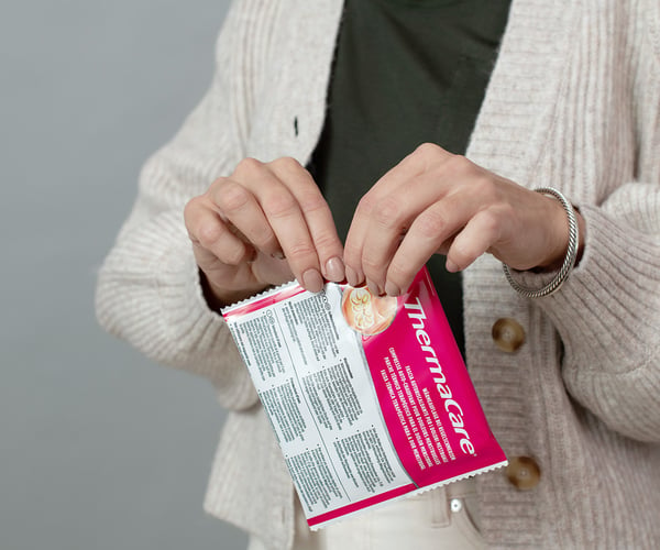 Frau öffnet Verpackung einer ThermaCare® Wärmeauflage bei Regelschmerzen