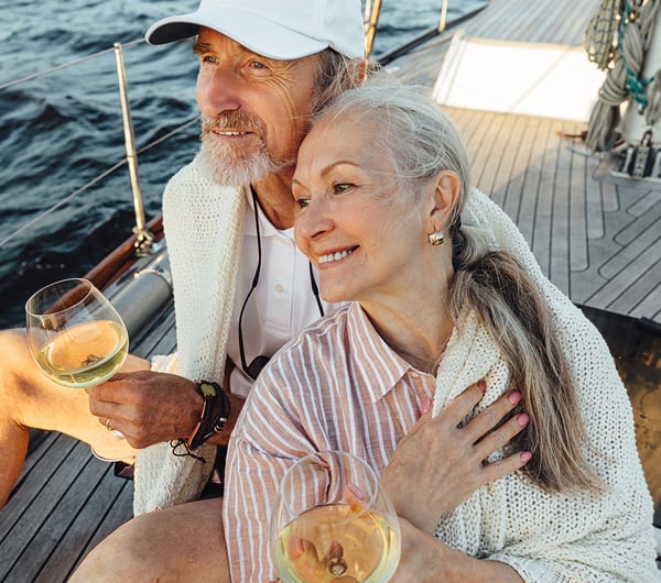 Ein Mann und eine Frau sitzen sich umarmend auf einem Schiff mit einem Glas Wein 