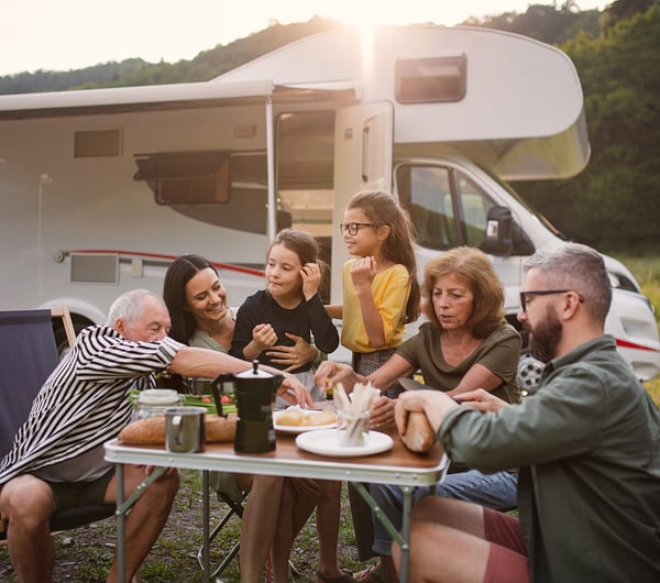 Eine Familie sitzen essend vor einem Camper am Tisch 