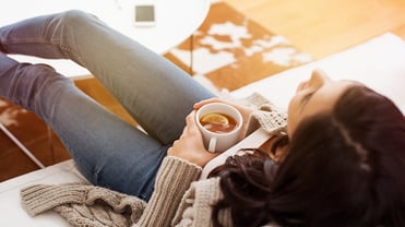 Eine Frau sitzt mit einer Tasse Tee in der Hand auf der Couch.